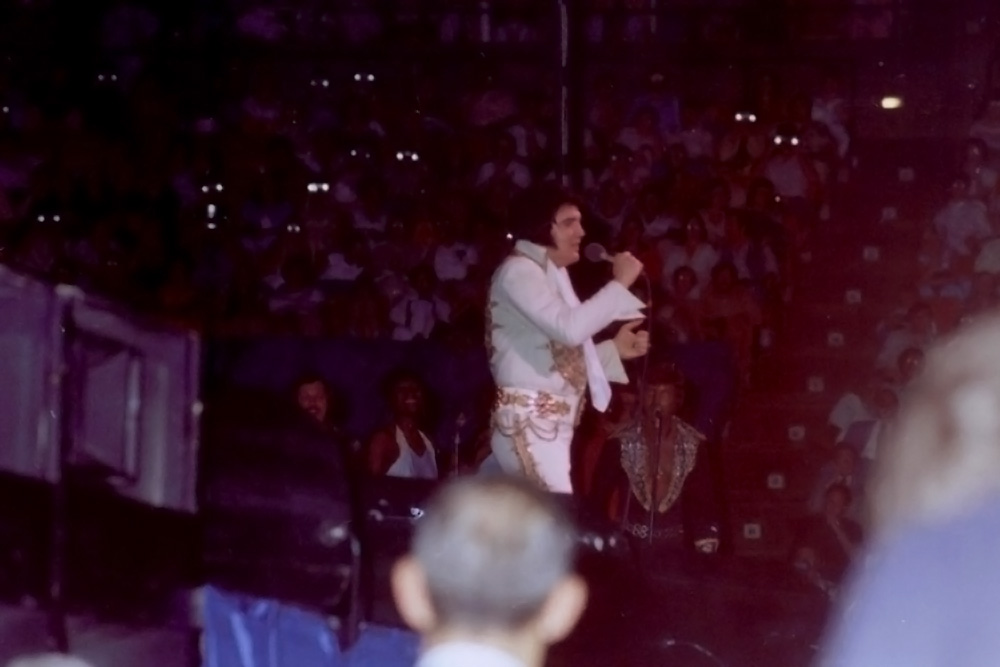 Elvis Presley auf der Bühne während seines letzten Konzerts am 26. Juni 1977 in Indianapolis, gekleidet in seinem weißen Mexican Sundial Suite. Dieses emotionale Konzert markierte das Ende einer legendären Live-Karriere.